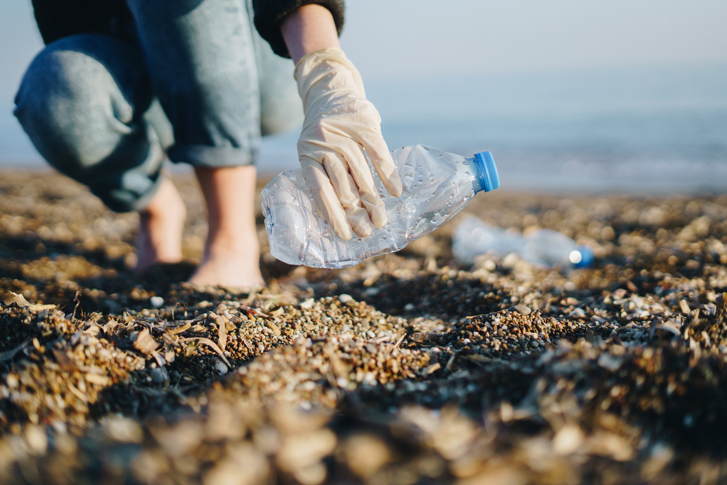 Woman volunteer cleaning up beach, picking up plastic bottles