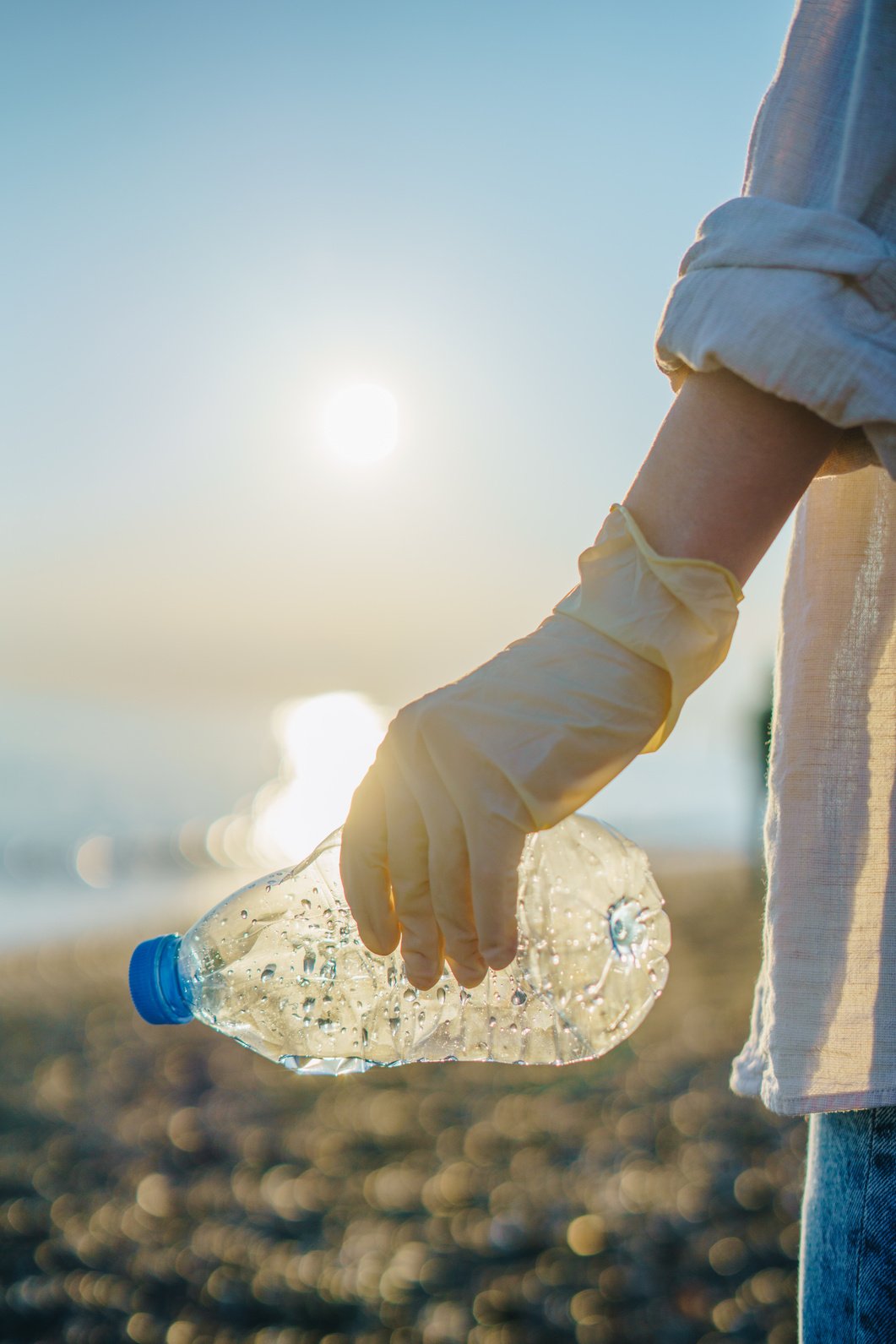 Woman volunteer cleaning up beach, picking up plastic bottles